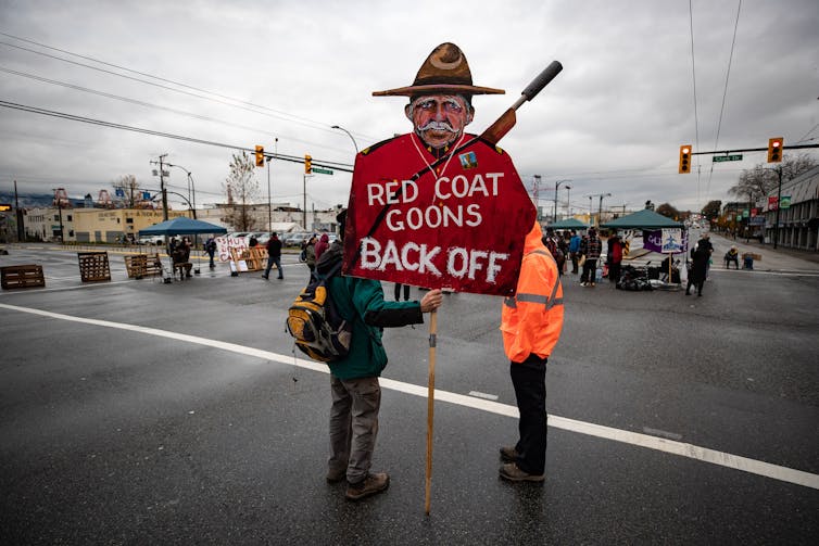 A demonstrator holds a sign with a caricature of an RCMP officer