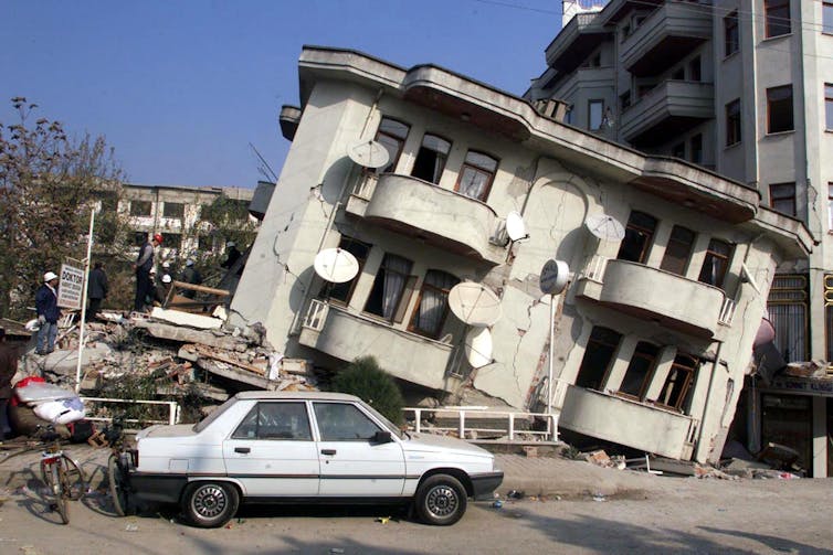 A car is parked outside a building that has subsided on one side.