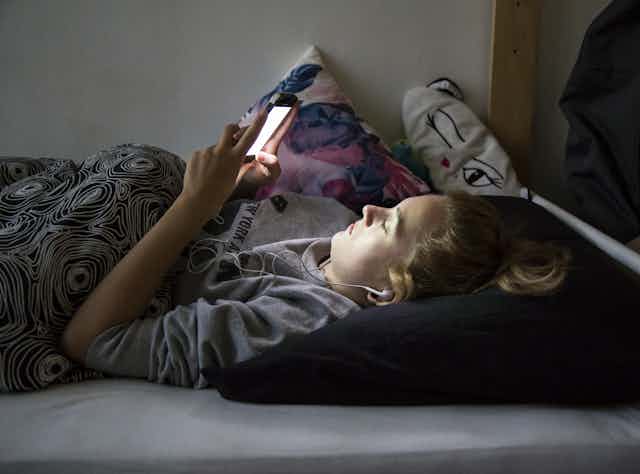 a teen lies on a bed staring up at their screen
