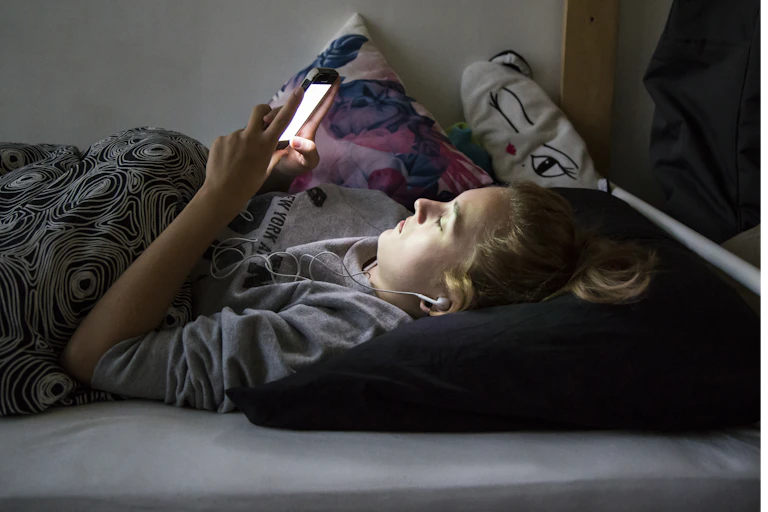 a teen lies on a bed staring up at their screen