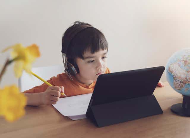 young child sits at laptop with headphones on