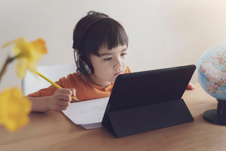 young child sits at laptop with headphones on