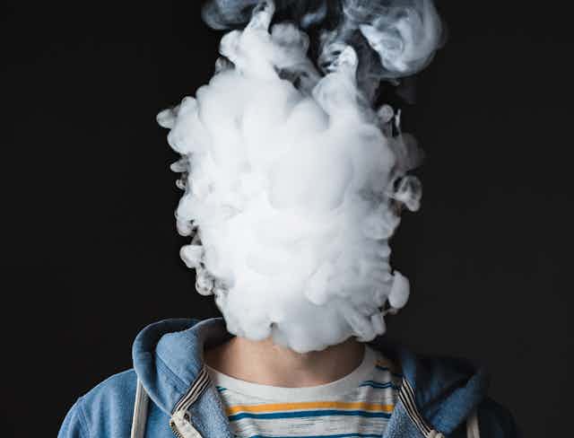 A person with their head obscured by a cloud of smoke against a back background