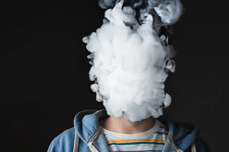 A person with their head obscured by a cloud of smoke against a back background