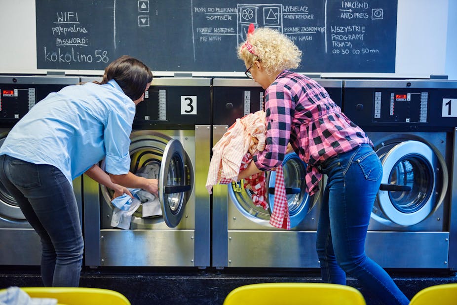 Two women loading washing into washing machines at a laundrette.