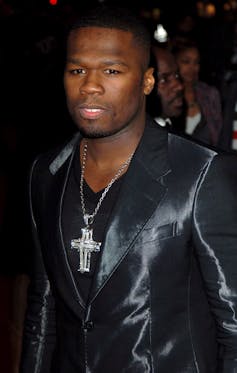 50 Cent wearing a shiny black jacket, black t-shirt and large crucifix chain.