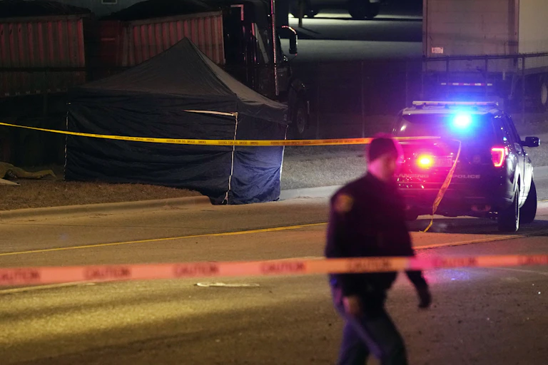 A police officer walks in front of a police car and a dark-colored tent.