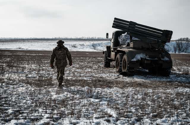 Soldat près d'un véhicule d'artillerie dans un champ enneigé.