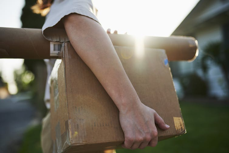 A person walks while holding two packages under his arm.