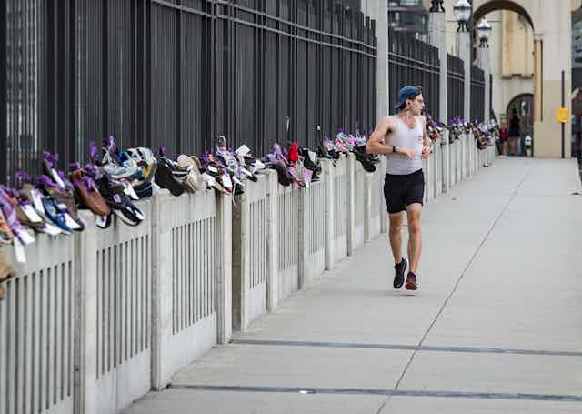 A man runs along a bridge with dozens of pairs of shoes tied to the barricades.