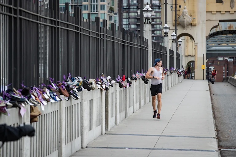 A man runs along a bridge with dozens of pairs of shoes tied to the barricades.
