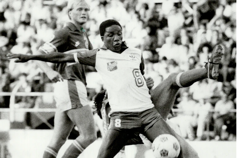 A Black soccer player holds off other players while the ball bounced in front of him.