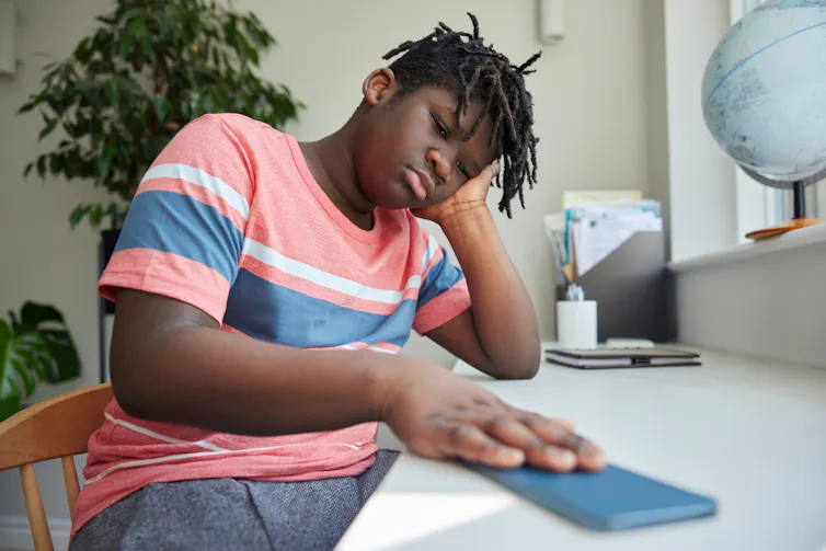 a young sad-looking boy pushes a phone away