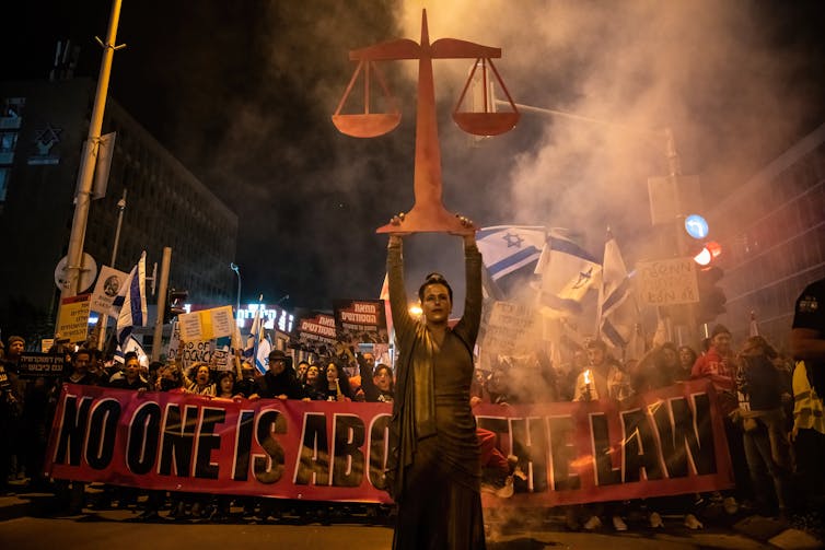 A protester raises a 'Scales of Justice' symbol while other protesters hold a banner and placards during a demonstration
