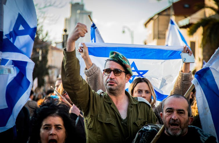 A man marching in a protest wearing a military uniform raises his fist.