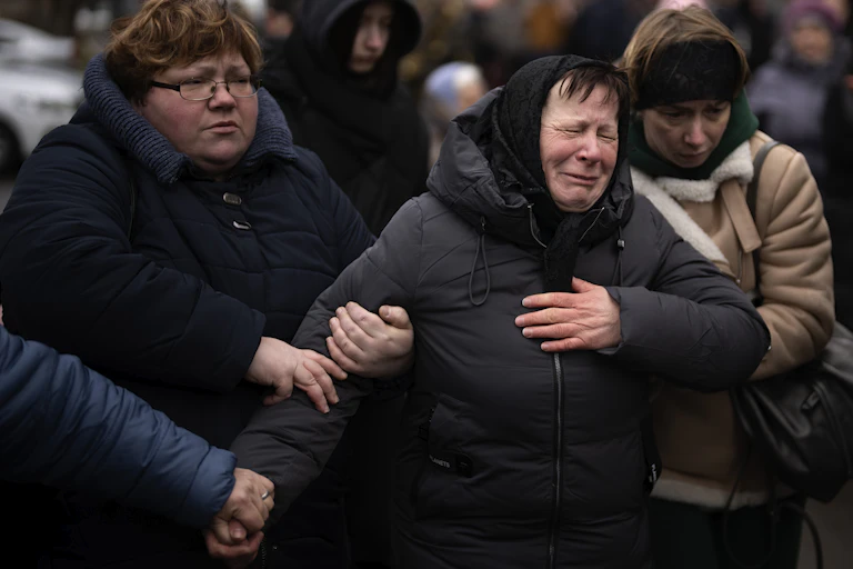 A woman in a black headscarf sobs as two women on either side hold onto her.