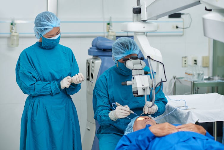 A patient lies on a gurney as a doctor performs surgery on their eye.
