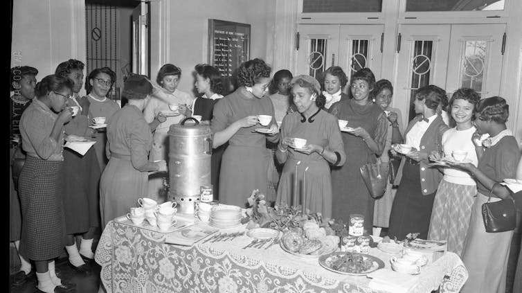 Women in formal and office attire a a party in the mid-20th century, in a black and white photograph
