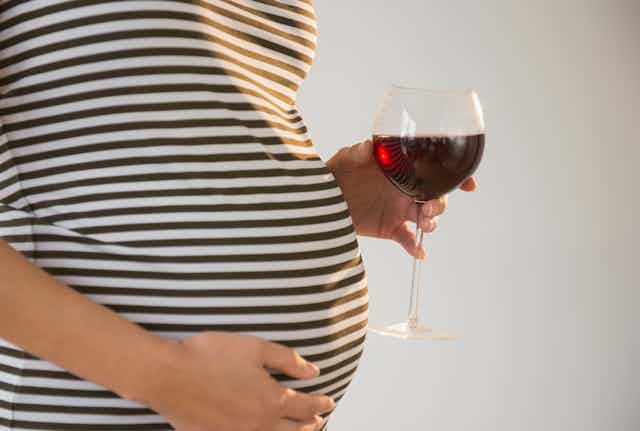 pregnant person holds glass of wine