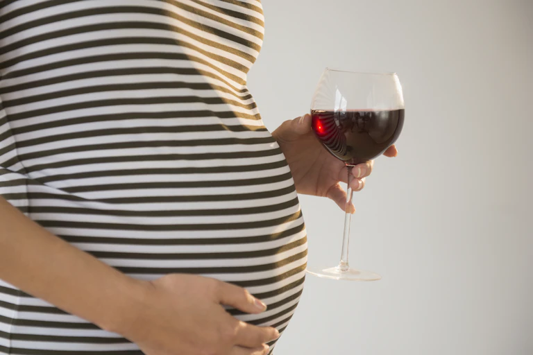 pregnant person holds glass of wine