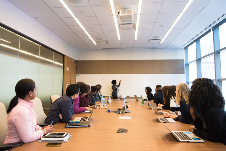 A meeting room with a table and people on both sides of it, taking notes on books and laptops