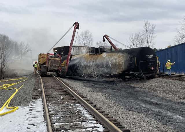 Workers use cranes to remove burned train cars 