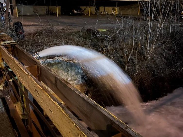 A stream of water, as from a fire hose, pours into a creek.