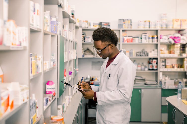 A young male pharmacist makes notes on a clipboard.