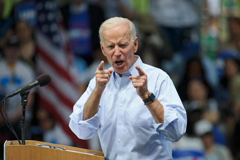 A man facing the camera in shirt sleeves standing next to a microphone.