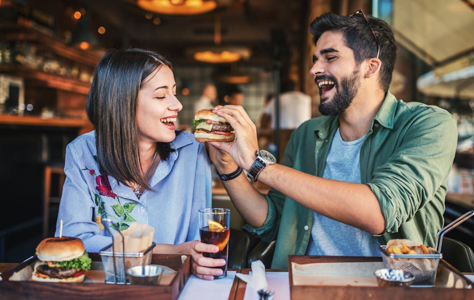 A young couple sat in a restaurant eating a burger.