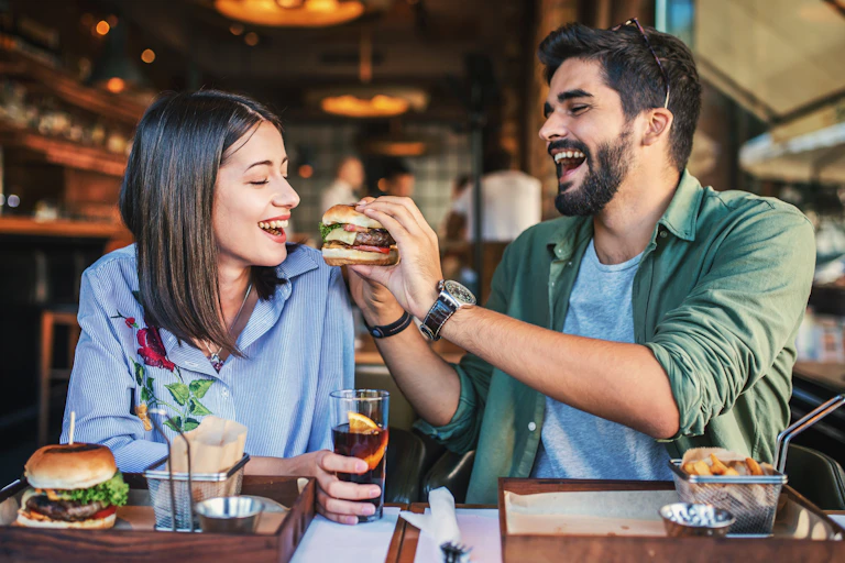 A young couple sat in a restaurant eating a burger.