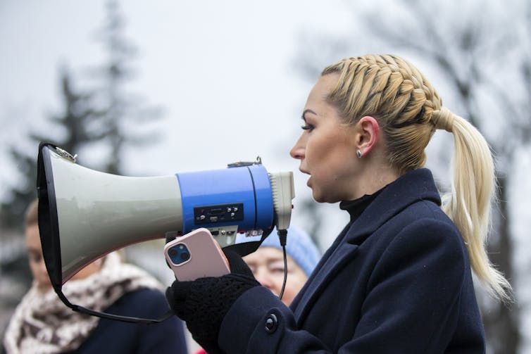 A blonde woman speaks into a loudhailer