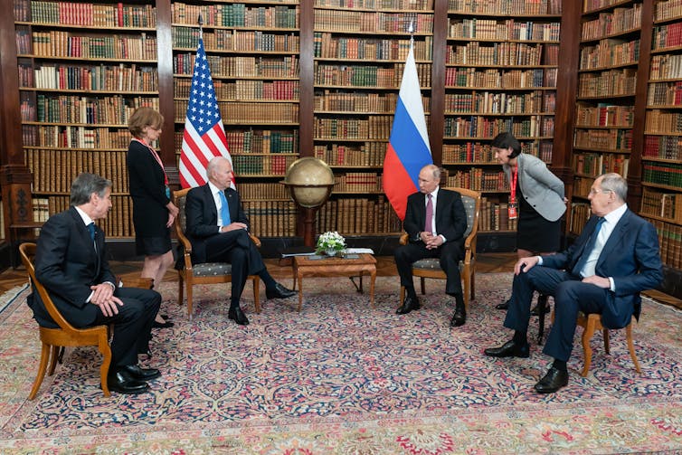Four men sat across from each other, the Russian and US flags in the background.