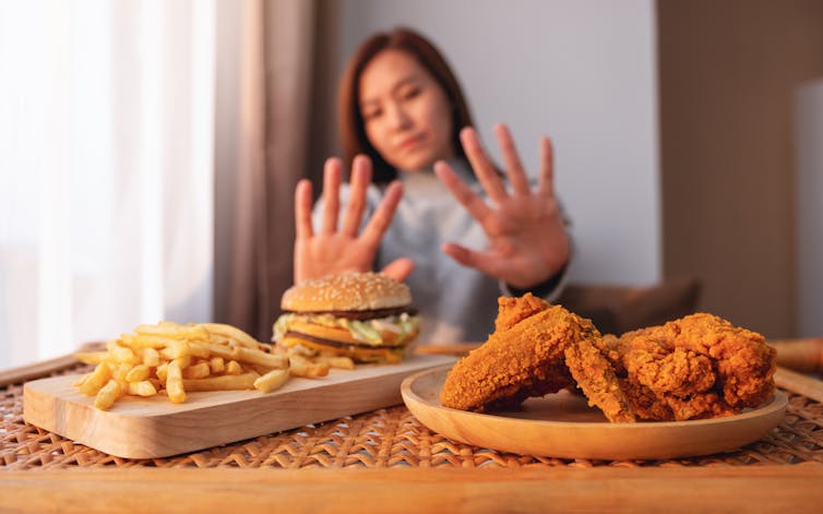 A woman making a hand sign to refuse a hamburger, french fries and fried chicken.
