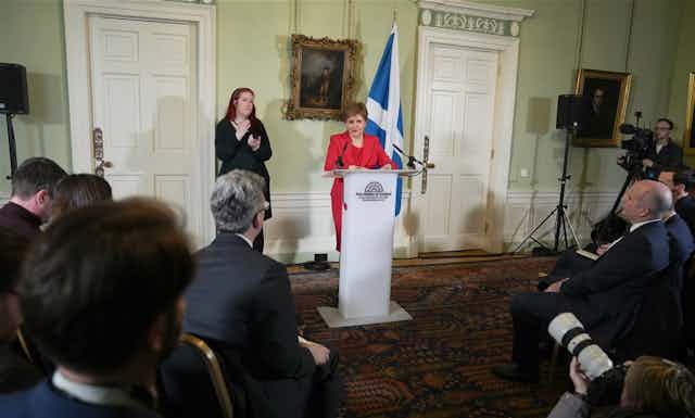 Wide shot of Nicola Sturgeon delivering her resignation speech from a podium to a room of reporters