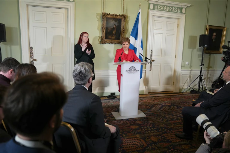 Wide shot of Nicola Sturgeon delivering her resignation speech from a podium to a room of reporters