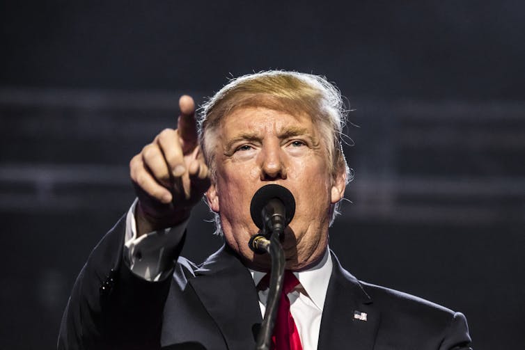 Close up of Donald Trump speaking into a microphone and pointing