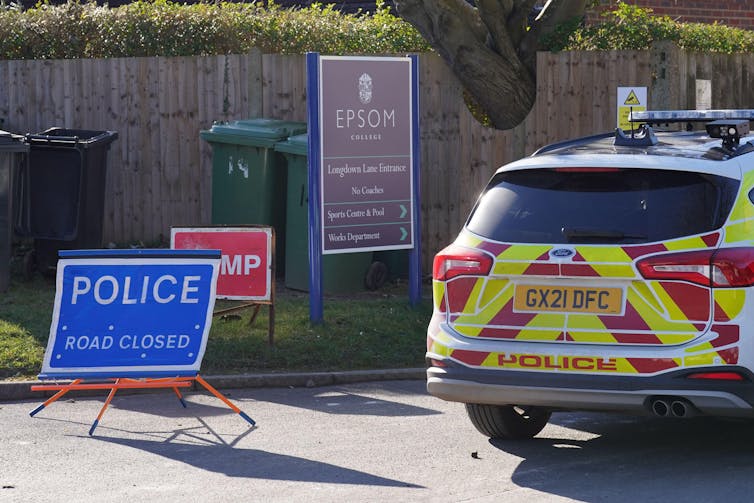 A police car and signage next to an entrance sign at Epsom college