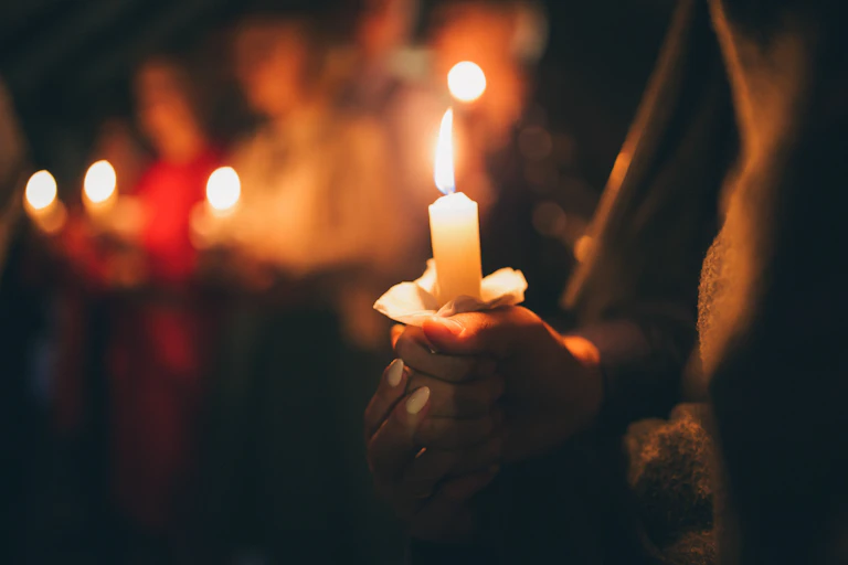 Close up photo of a woman holding a lit candle at a vigil