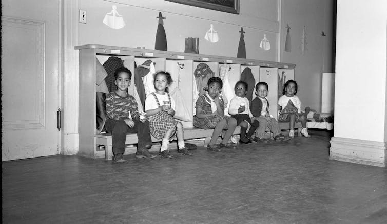 Black and white photo of children sitting on a bench wearing old-fashioned clothing