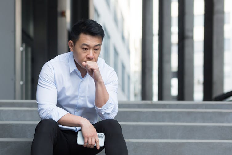 a man sits on steps with his hand held to his mouth