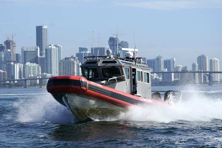 A boat through a large body of water with a city skyline visible in the background