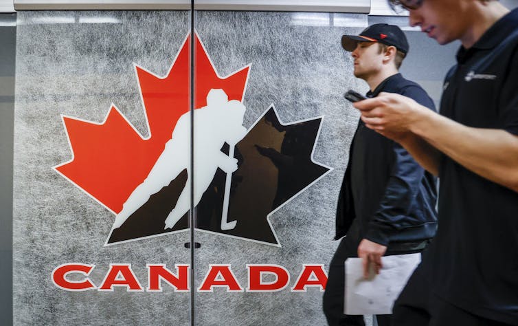 People walk past a door with the Hockey Canada symbol. A red and black maple leaf with a hockey player.