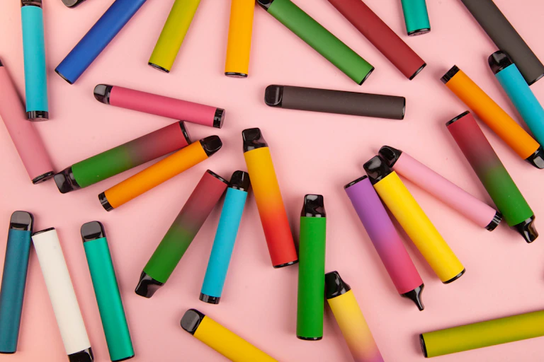 Disposable coloured e-cigarettes of different flavours on a pink surface