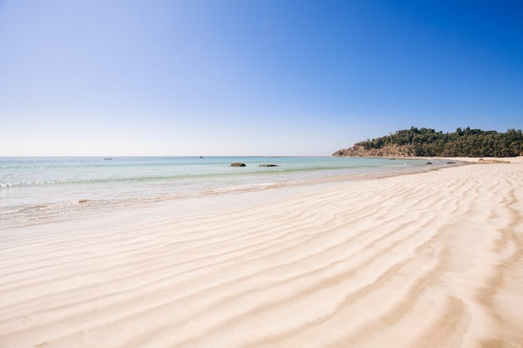 Sandy beach, blue sky, headland in distance