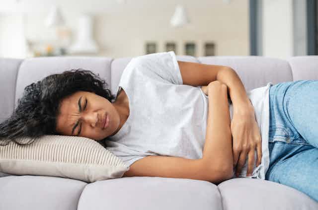 A woman lying on the couch clutching her stomach.