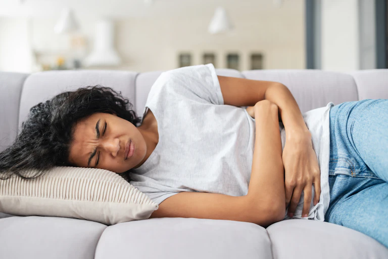 A woman lying on the couch clutching her stomach.
