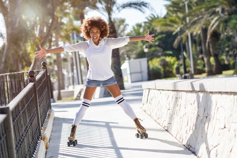 A girl in jean shorts and a white tee rollerskating outdoors.