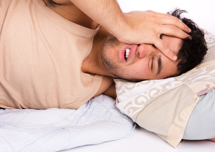 Un uomo stanco che giace a letto si mette una mano sul viso per la frustrazione, incapace di dormire.