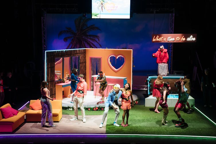 young people embrace, cavort and chat on the stage of Much Ado About Nothing, in bright clothing.